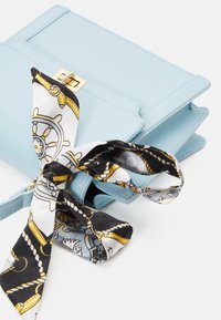 Ljusblå läderhandväska med en strukturerad design, prydd med ett guldhardware-spänne och en svartvit mönstrad silkescarf knuten runt den.