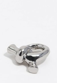 Accessorio metallico a forma di anello con finitura lucida e riflettente in argento, caratterizzato da una parte superiore arrotondata e due accenti sporgenti.