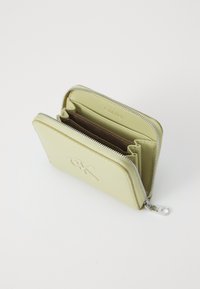 Kompakt lys grønn Calvin Klein-lommebok med glidelås åpen, som viser flere kortlommer og rom inni.