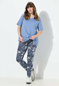 Camisa de algodón azul clara de manga corta combinada con leggings navy que presentan un patrón floral en espiral en blanco. El modelo lleva zapatillas blancas.