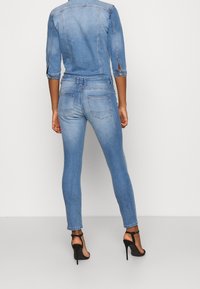 Světle modré džíny s úzkým střihem, pěti kapsami a jemnými detaily v prošívání. V kombinaci s černými sandály na vysokém podpatku.