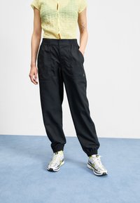 Black, lightweight sweatpants with elastic waistband and cuffs; paired with a textured yellow top and gray sneakers with yellow accents.