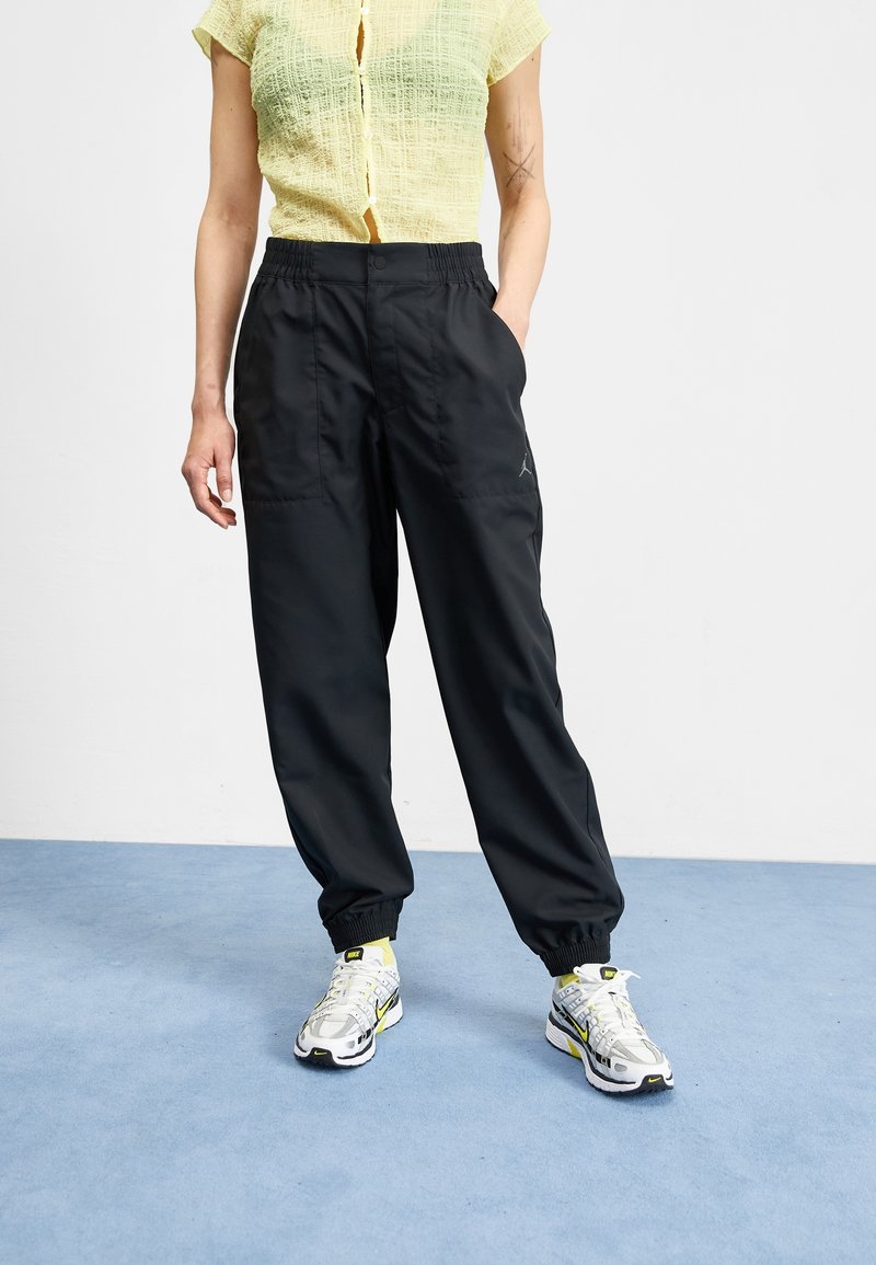 Black, lightweight sweatpants with elastic waistband and cuffs; paired with a textured yellow top and gray sneakers with yellow accents.