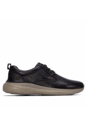 Zapato bajo de cuero negro con suela de goma beige texturizada, cierre de cordones en la parte delantera y lengüeta en el talón, mostrado en perfil lateral derecho.