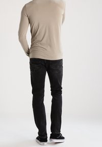 Beige långärmad skjorta, figursydd, kombinerad med svarta jeans med fickor och en lätt blekning, fulländad med svarta sneakers.