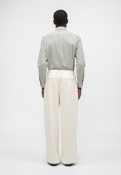 Svītrains garo piedurkņu krekls bēšā un pelēkā krāsā, apvienots ar platām krēmkrāsas biksēm. Gluda tekstūra ar detalizētu šuvju izšuvumu uz biksēm.