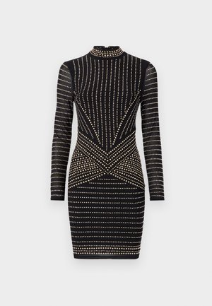 Rochie neagră cu mâneci lungi și guler înalt, decorată cu cuie aurii dispuse în modele verticale și orizontale, evidențiind o siluetă ajustată.