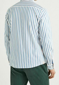 Camisa blanca de manga larga con rayas verticales azules, con cuello y puños abotonados, elaborada en tela texturizada.