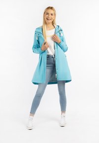 Cămașă de ploaie bleu deschis cu glugă, accesorii argintii, manșete elastice și ciucuri albi. Asortată cu o cămașă albă, blugi deschiși și pantofi sport.