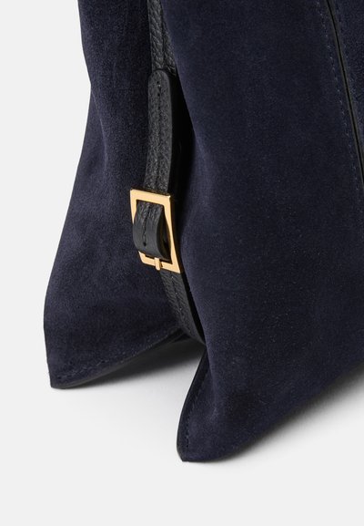 Bolsa de mão em camurça azul-marinho com superfície texturizada, pormenores em couro preto e um detalhe de fivela quadrada dourada na alça.