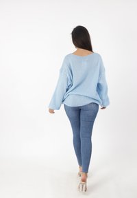 Lichtblauwe oversized gebreide trui met lange mouwen, V-hals en textuurstof, gecombineerd met slim-fit donkere spijkerbroek en doorzichtige hakken.