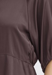 Lilla satin top med en afslappet pasform, der har pufærmer og en elastisk talje for at definere formen. Glat tekstur uden synlige mønstre.
