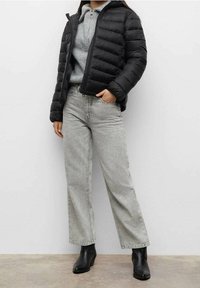 Svart puffjacka med horisontellt quiltat mönster, grå tröja under, ljusgrå vida jeans och svarta ankelstövlar.