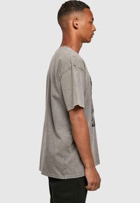 Grey cotton T-shirt with a relaxed fit, short sleeves, and a side seam design. Faded texture and black graphic print on front.