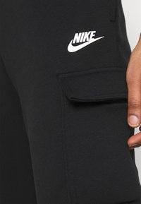 Černé bavlněné joggers s postranní kapsou na cargo a bílým logem Nike na stehně. Měkká textura a uvolněný, pohodlný střih.