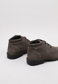 Botas de tobillo de ante gris con suelas de goma negra, que cuentan con cierre de cordones, detalles de costura y un logo sutil en el lateral.