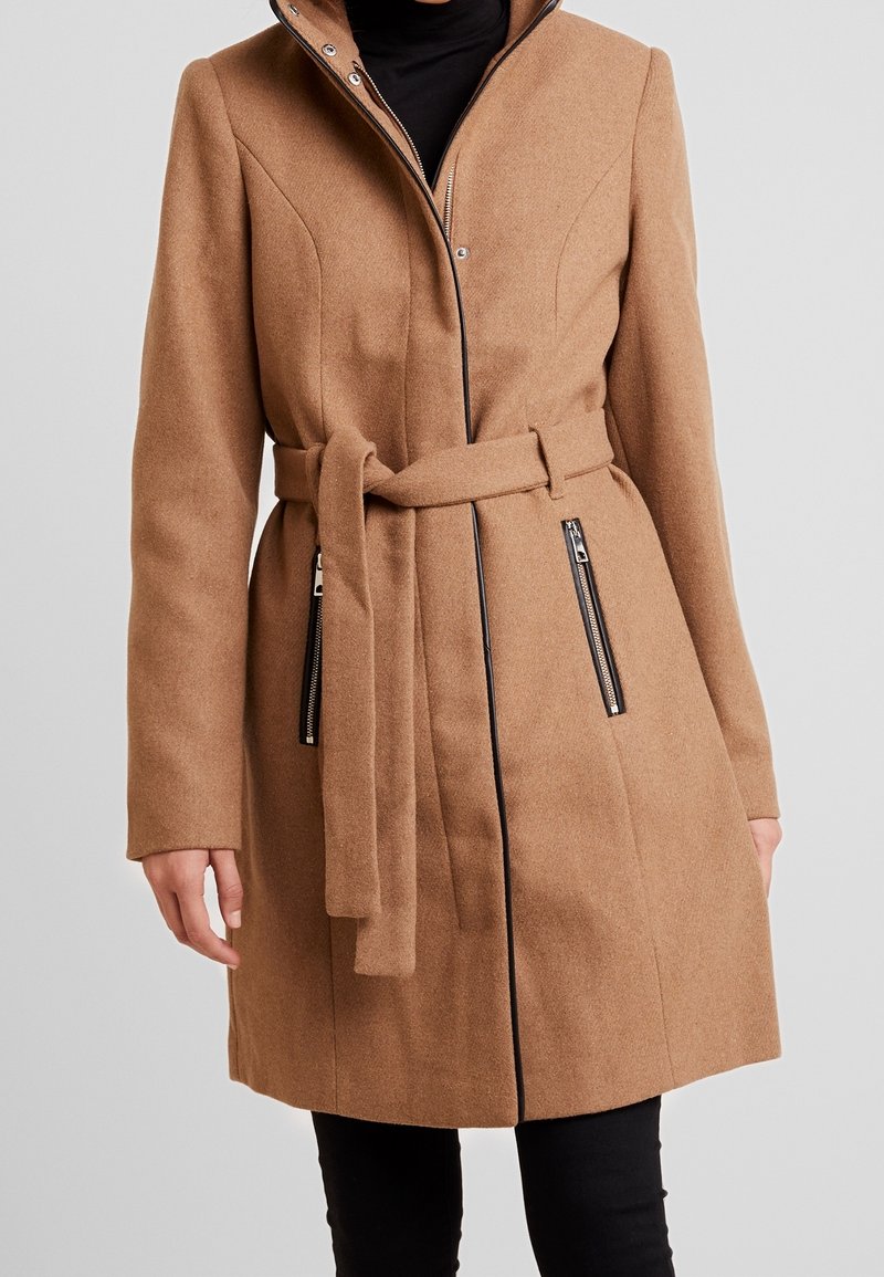 Ruskea villa-sekoituksesta valmistettu takki, jossa on vyötärölle sidottava vyö, vetoketjulliset taskut ja korkea kaulus, joka tarjoaa sileän pinnan ja muotonsa mukaisen istuvuuden.