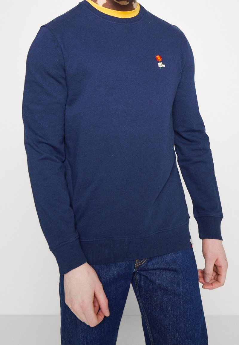 Navy blue sweatshirt made of cotton, featuring long sleeves, a ribbed crew neckline, and a small embroidered rose detail on the chest.