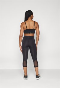 Svart sports-BH med justerbare stropper og subtil teksturert mønster, sammen med svarte capris som har mesh-paneler på de nedre bena.
