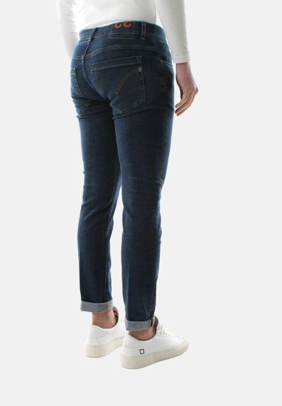 Jeans in denim blu scuro con vestibilità slim, caratterizzati da orli risvoltati, dettagli di cucitura arancione e tasche posteriori. Abbinati a sneakers bianche.