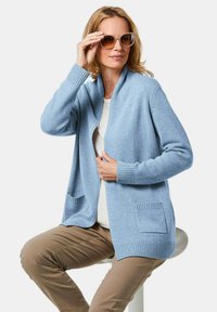 Helles blauer Cardigan mit Schalkragen, strukturiertem Strickstoff und gerippten Bündchen. Verfügt über zwei vordere Taschen für zusätzlichen Details.