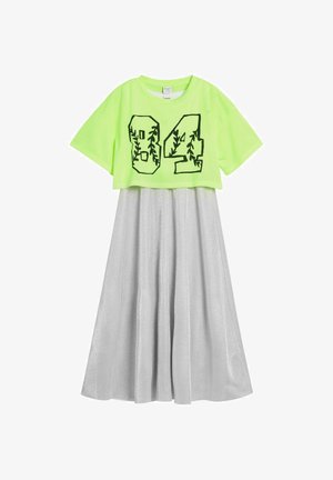 Neónovo zelené priesvitné krátke tričko so sieťovinou s číslom "04" a motívom viniča cez strieborné plisované midi šaty s lesklou textúrou.