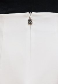 Ασημένιο τράβηγμα φερμουάρ με κείμενο "HUGO" σε μαύρο και λευκό υφασμάτινο ένδυμα με υφή, το φερμουάρ είναι μερικώς κλειστό στη μεσαία ραφή.