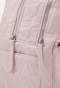 Ljusrosa vadderad ryggsäck med silverfärgade dragkedjor, som har geometriska sömmönster och en liten framsida med läderfransar.