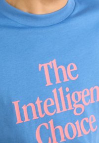 Světle modré bavlněné tričko s velkým růžovým nápisem „The Intelligent Choice“. Látka má jemnou strukturu a volný střih.