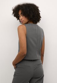 Haut sans manches gris avec un col haut, un design structuré et une texture lisse. La vue de dos montre des coutures minimales et une coupe ajustée.