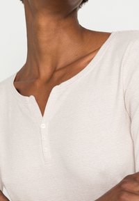 Helles beige Henley-Oberteil mit einem strukturierten, gerippten Muster, runder Halslinie und drei kleinen Knöpfen an der Front.