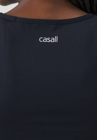 Bakifrån på en person som bär en svart topp med "casall"-logotypen tryckt i vitt i den övre mitten av ryggen.