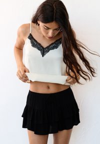 Camicetta bianca con rifiniture in pizzo nero, abbinata a una mini gonna nera a volant e a balze. L'outfit presenta una vestibilità comoda e un elastico in vita con cordino.