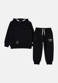 Sweat à capuche noir pour enfants avec poche avant et pantalon cargo doté d'une taille élastique et de cordons blancs, tous deux ornés de petites étiquettes de marque.