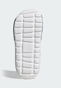 Biała gumowa podeszwa buta z teksturowanymi rowkami i wypustkami; na środku znajduje się wytłoczone logo. Projekt zapewnia przyczepność i stabilność.
