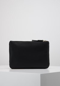 Czarna skórzana kopertówka o gładkiej fakturze, z zamkiem błyskawicznym i minimalistycznym, prostokątnym kształtem. Posiada małą skórzaną pętlę do uchwytu.