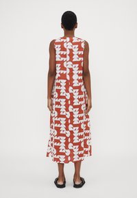 Maxiklänning med ett röd- och vitt geometriskt mönster. Ärmlös design, fladdrande tyg och längd till mitten av vaden. Inga synliga stängningar.