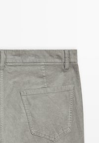 Pantaloni in corduroy grigio con una cintura strutturata, una tasca posteriore e una texture a righe verticali. Design semplice con un colore tenue.
