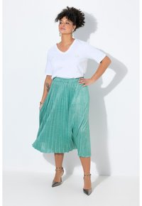 T-shirt bianco con scollo a V e decorazioni, abbinato a una gonna midi plissettata color teal in tessuto lucido e scarpe con tacco alto argento.
