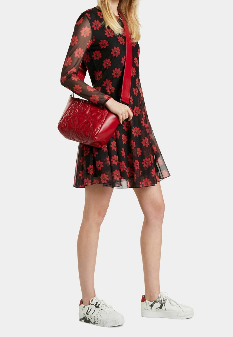Červená kabelka s květinovým vzorem, spárovaná s černými šaty s červenými květy a bílými teniskami s kreslenou postavičkou.