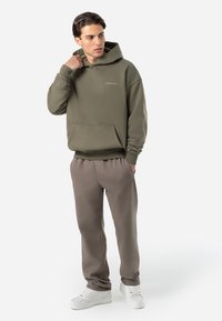 Olivengrøn hættetrøje med en kængurulomme, ribbede manchetter og et logo. Sammen med lysegrå sweatpants og hvide sneakers.