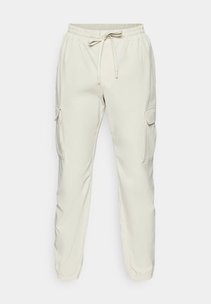 Pantalons cargo beiges avec une taille élastique, détails à cordon de serrage et deux poches cargo latérales. Tissu lisse avec un design de jambe fuselée.