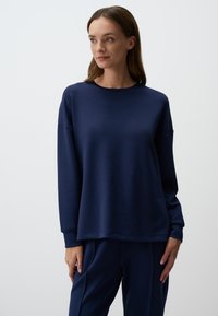 Felpa blu navy in morbido materiale, con maniche lunghe, collo rotondo e vestibilità comoda. Abbinata a pantaloni coordinati.