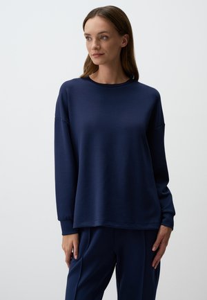 Navy blue sweatshirt in soft material with long sleeves, a round neckline, and a relaxed fit. Paired with matching pants.