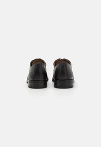 Zapatos de vestir de piel negra con una superficie suave, punta redonda y tacón bajo, con un sutil logo en la parte trasera.