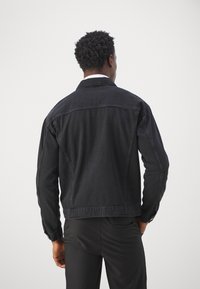 Zwarte denimjack met een ontspannen fit, achterste naden en een klassieke kraag. Beschikt over lange mouwen en een gestructureerde afwerking.