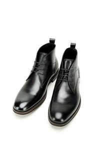 Botas de tobillo de cuero negro con paneles laterales texturizados, un acabado suave, punta estrecha y lengüetas en la parte superior para facilitar su uso. Diseño clásico con cordones.