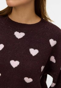 Pull en tricot bordeaux avec des motifs de cœurs roses clair dispersés et un col côtelé. Texture douce avec une coupe décontractée.
