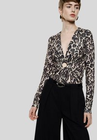 Top a maniche lunghe con stampa leopardata, caratterizzato da una profonda scollatura a V e un dettaglio centrale a nodo circolare, abbinato a pantaloni neri a vita alta con cintura.