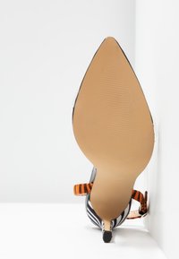 Escarpin à talon haut rayé noir et blanc avec bout pointu et bride de cheville rayée orange et noir, vu de la semelle.